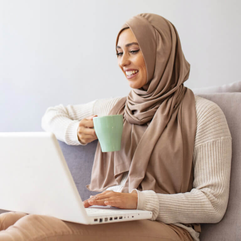 young woman holding a cup using laptop
